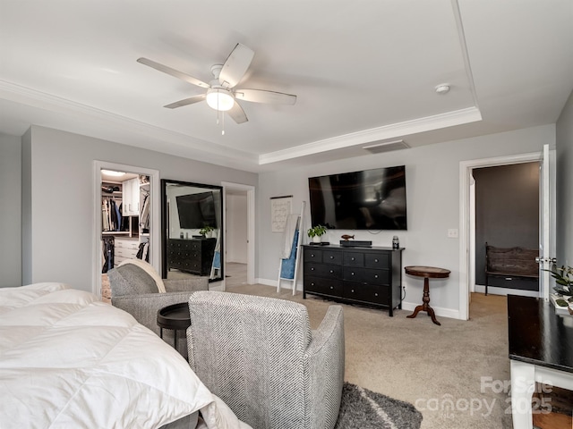 bedroom with ceiling fan, light colored carpet, a tray ceiling, and a spacious closet