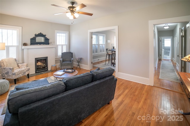 living room featuring ceiling fan, a healthy amount of sunlight, a fireplace, and light hardwood / wood-style floors