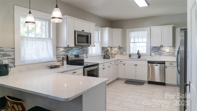 kitchen featuring appliances with stainless steel finishes, white cabinetry, sink, hanging light fixtures, and kitchen peninsula