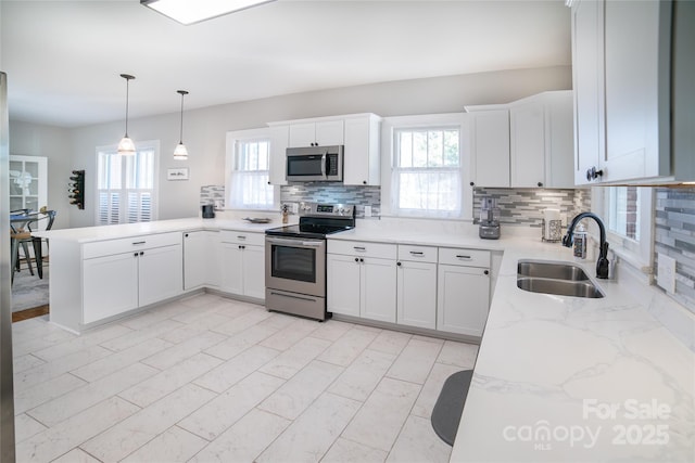 kitchen featuring sink, backsplash, stainless steel appliances, white cabinets, and decorative light fixtures