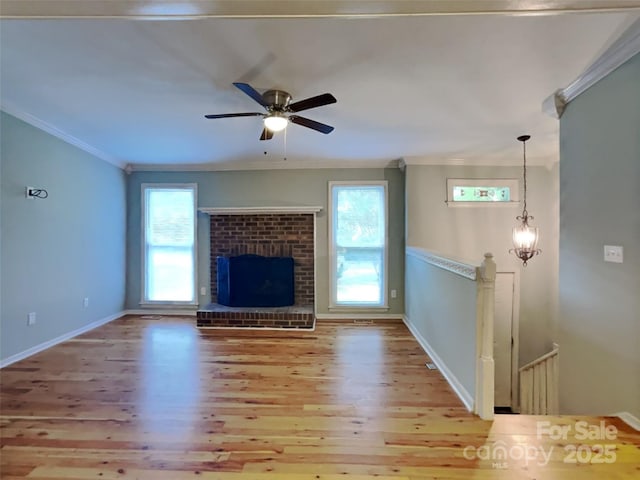 unfurnished living room featuring ceiling fan with notable chandelier, ornamental molding, a fireplace, and light hardwood / wood-style floors