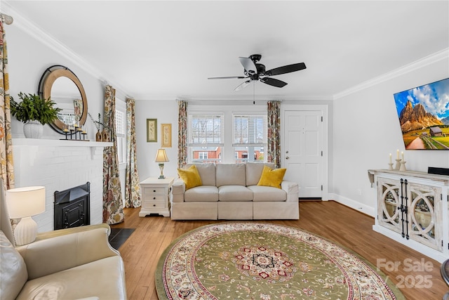 living room with a fireplace, ornamental molding, ceiling fan, and light wood-type flooring