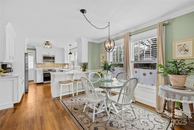 dining space with crown molding, sink, hardwood / wood-style floors, and a notable chandelier