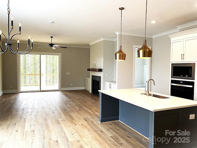 kitchen featuring sink, an island with sink, built in microwave, decorative light fixtures, and oven