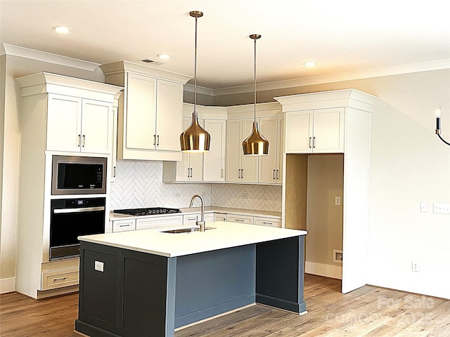 kitchen featuring built in microwave, sink, oven, stainless steel gas cooktop, and a center island with sink