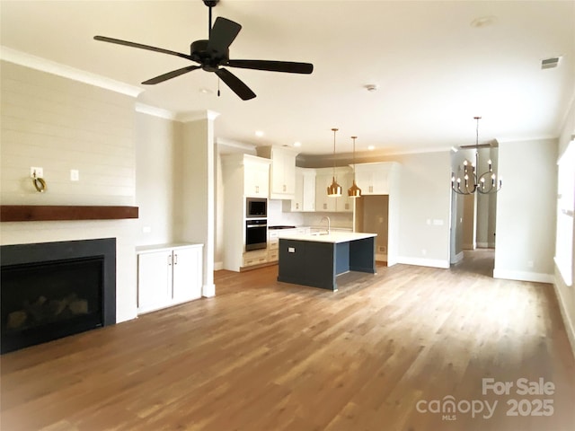 kitchen featuring white cabinetry, hanging light fixtures, a center island with sink, ornamental molding, and oven