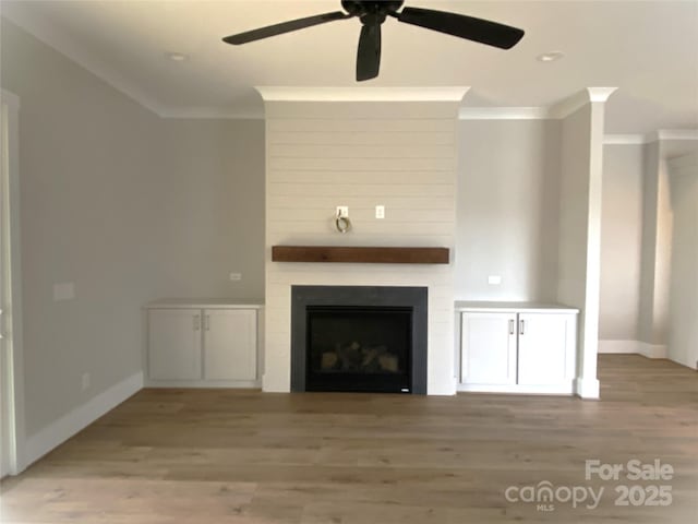 unfurnished living room with crown molding, a large fireplace, hardwood / wood-style floors, and ceiling fan