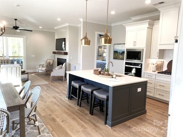 kitchen with stainless steel microwave, open floor plan, oven, white cabinetry, and a sink