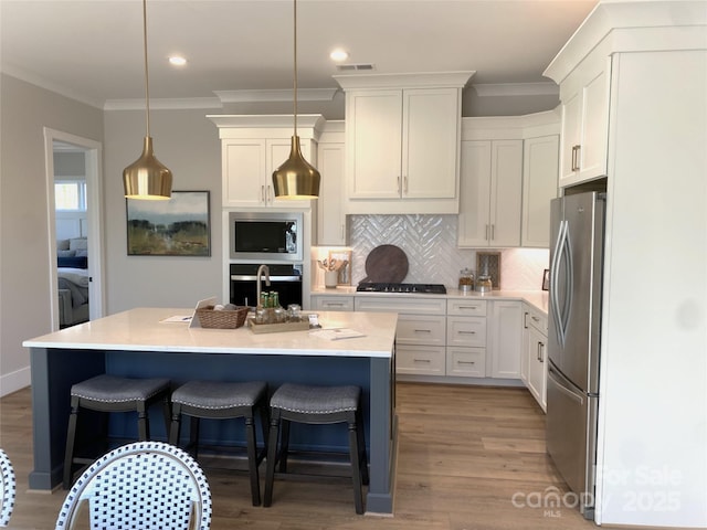 kitchen with a breakfast bar area, stainless steel appliances, tasteful backsplash, ornamental molding, and white cabinetry