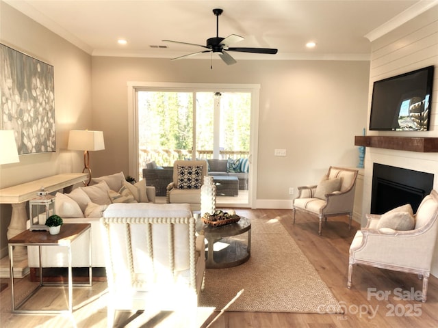 living area featuring a large fireplace, wood finished floors, visible vents, baseboards, and ornamental molding