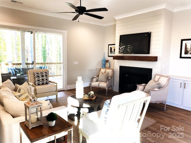 living room with ornamental molding, a ceiling fan, a large fireplace, wood finished floors, and baseboards