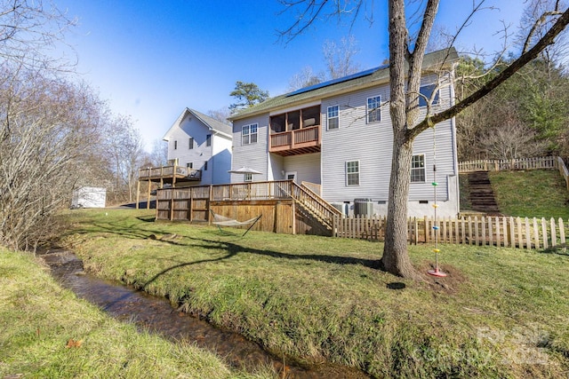 rear view of house with central AC unit, a deck, and a lawn