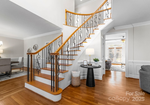 stairs with ornamental molding, wood finished floors, a high ceiling, and a decorative wall