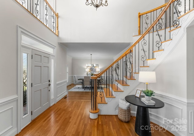 foyer entrance featuring a towering ceiling, an inviting chandelier, light wood-style flooring, and stairway