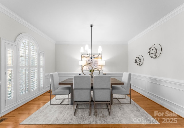 dining room with ornamental molding, a wainscoted wall, a notable chandelier, and light wood-style flooring