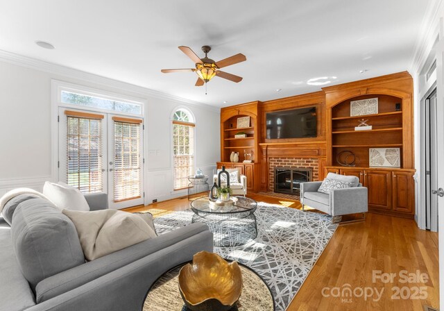 living room featuring a brick fireplace, ornamental molding, light wood-style floors, and built in features