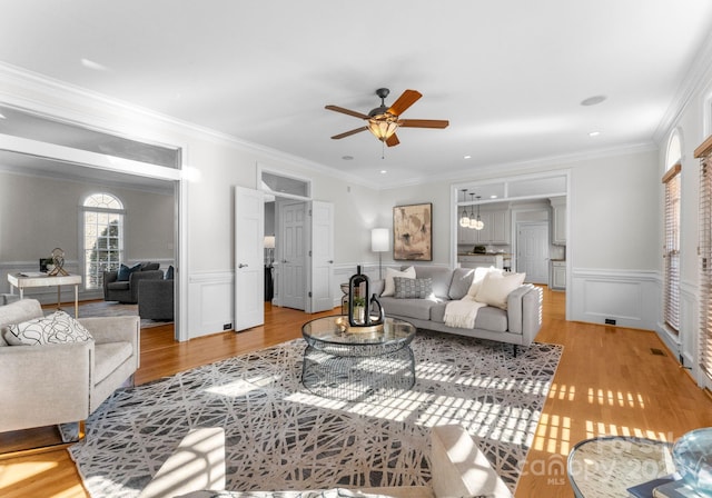 living area featuring light wood finished floors, ceiling fan, crown molding, and wainscoting