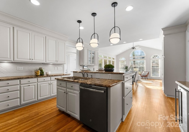 kitchen with lofted ceiling, decorative light fixtures, a sink, dishwasher, and a center island with sink