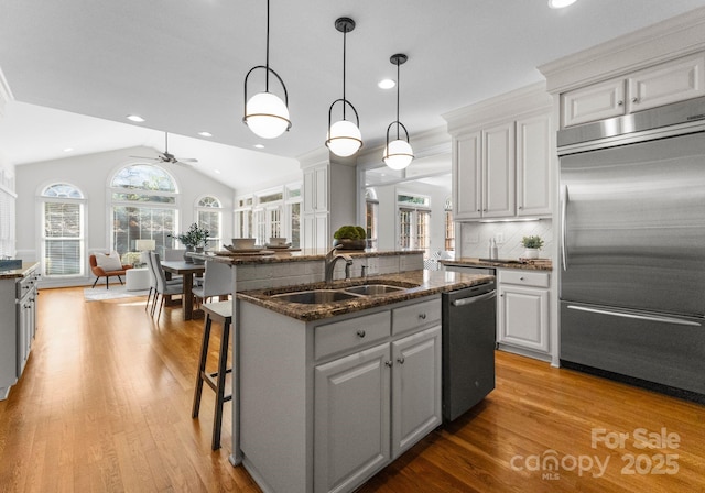 kitchen with a kitchen island with sink, stainless steel appliances, a sink, a kitchen breakfast bar, and decorative light fixtures