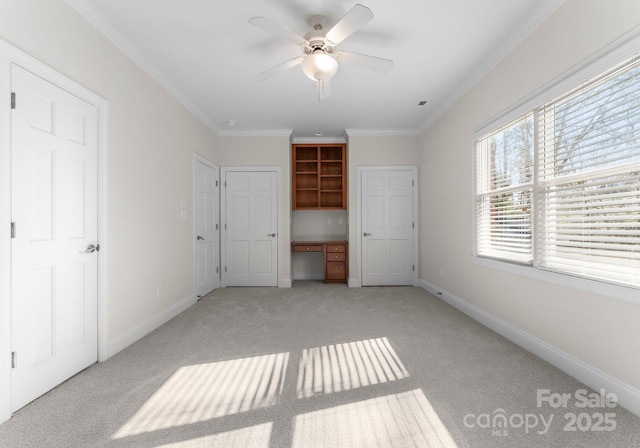 unfurnished bedroom with ornamental molding, built in study area, ceiling fan, light carpet, and baseboards