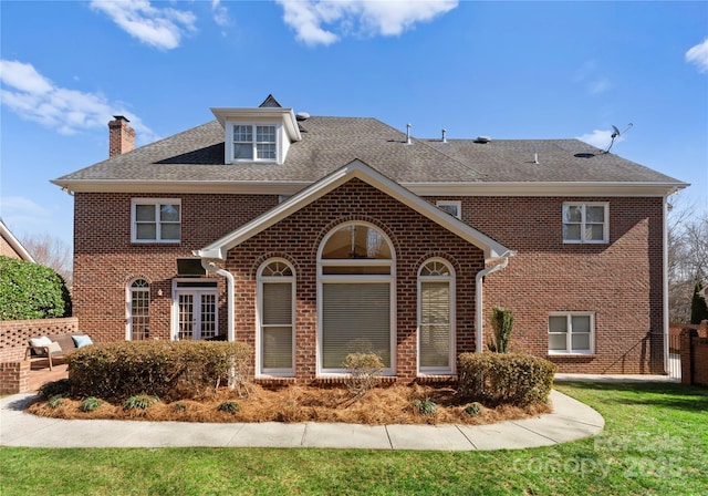 view of front of home with a shingled roof, a front lawn, a patio, and brick siding