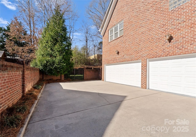 view of home's exterior featuring an attached garage, fence, concrete driveway, and brick siding