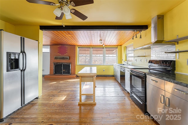 kitchen with wall chimney range hood, stainless steel appliances, a fireplace, decorative light fixtures, and light wood-type flooring