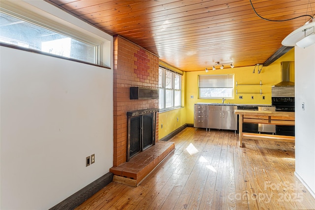 kitchen featuring sink, a brick fireplace, track lighting, hardwood / wood-style flooring, and wall chimney range hood