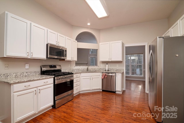 kitchen with sink, dark wood-type flooring, appliances with stainless steel finishes, white cabinetry, and light stone counters