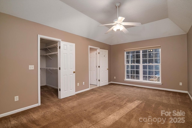 unfurnished bedroom with carpet floors, a walk in closet, vaulted ceiling, and ceiling fan