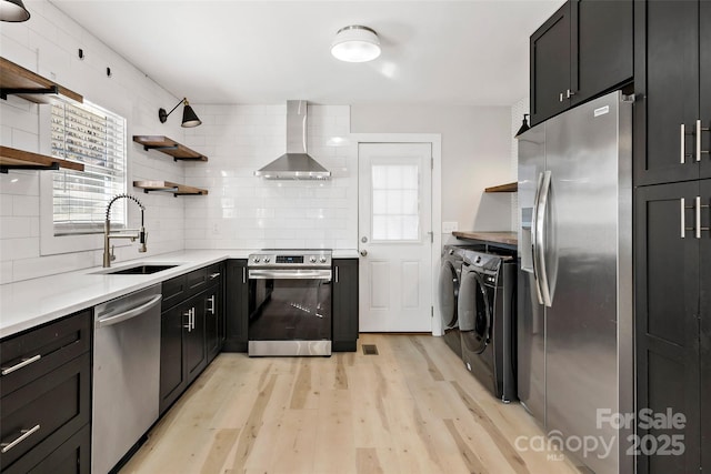 kitchen with sink, appliances with stainless steel finishes, backsplash, washer and dryer, and wall chimney exhaust hood