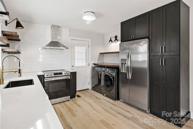 kitchen with appliances with stainless steel finishes, separate washer and dryer, sink, light hardwood / wood-style floors, and wall chimney range hood