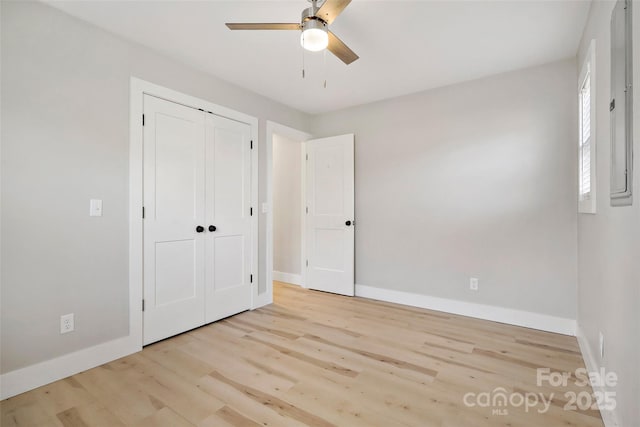 unfurnished bedroom with ceiling fan, electric panel, a closet, and light wood-type flooring