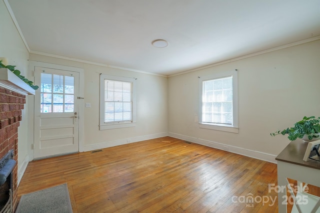 interior space with crown molding, a brick fireplace, a healthy amount of sunlight, and light wood-type flooring