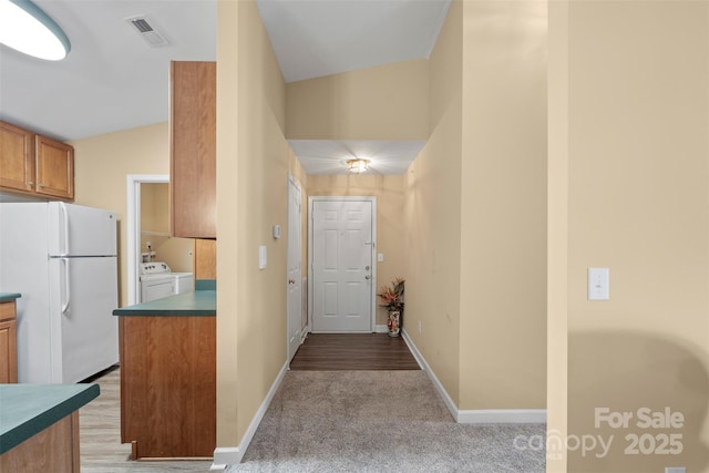 kitchen with white refrigerator, washer and clothes dryer, and light carpet