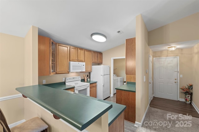 kitchen featuring white appliances, kitchen peninsula, washing machine and clothes dryer, and a breakfast bar