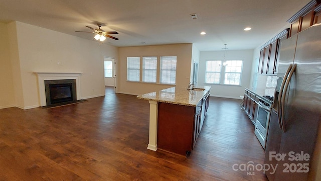 kitchen with pendant lighting, a kitchen island with sink, stainless steel appliances, light stone counters, and dark hardwood / wood-style flooring