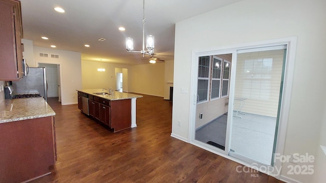 kitchen with light stone counters, dark hardwood / wood-style floors, a kitchen island with sink, and hanging light fixtures