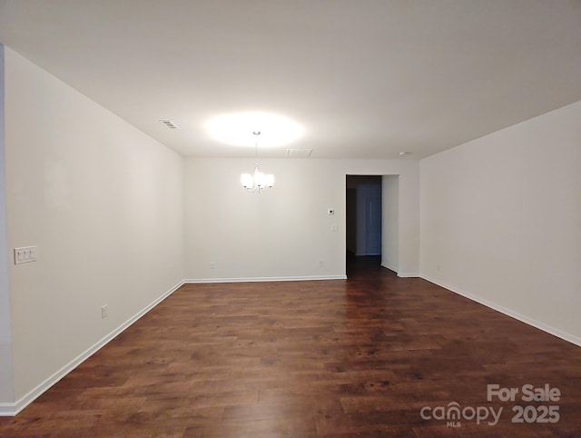 spare room with a notable chandelier and dark hardwood / wood-style flooring