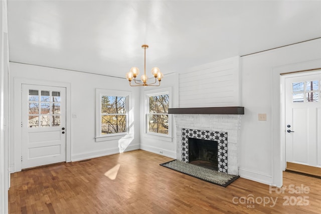 unfurnished living room featuring a brick fireplace, a healthy amount of sunlight, hardwood / wood-style floors, and a notable chandelier