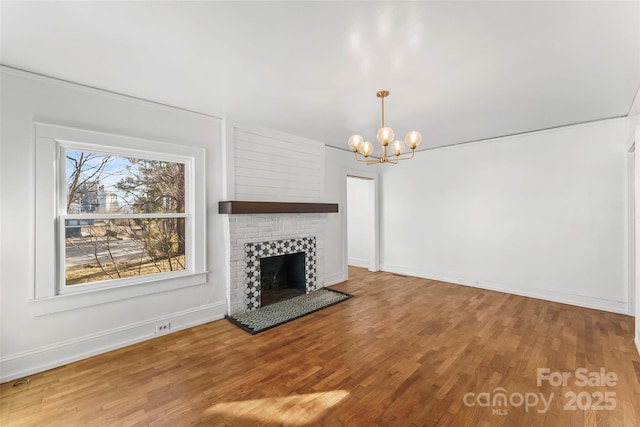 unfurnished living room featuring wood-type flooring, a brick fireplace, and a notable chandelier