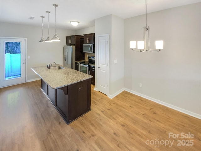 kitchen with sink, hanging light fixtures, dark brown cabinetry, stainless steel appliances, and a center island with sink