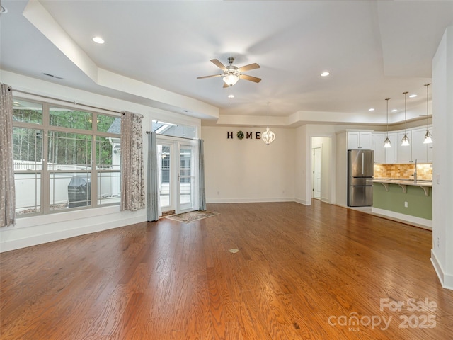 unfurnished living room with hardwood / wood-style flooring, a raised ceiling, and ceiling fan