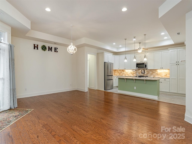 kitchen with a tray ceiling, a center island with sink, a breakfast bar area, and appliances with stainless steel finishes