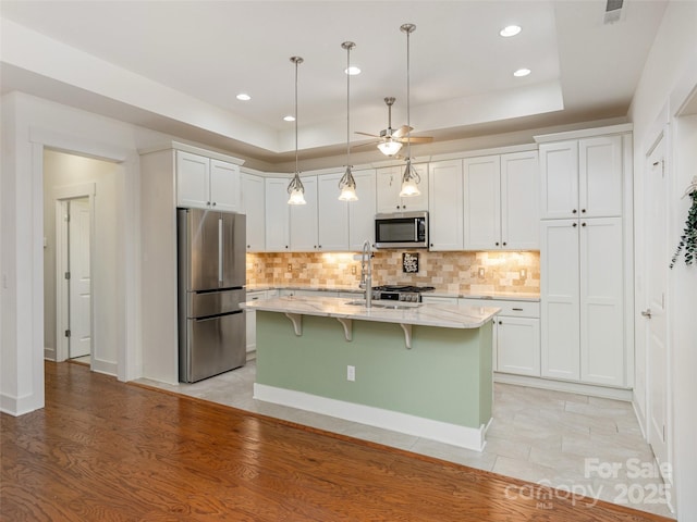 kitchen with white cabinetry, appliances with stainless steel finishes, a raised ceiling, and a center island with sink