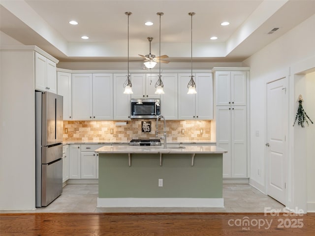 kitchen with pendant lighting, an island with sink, white cabinetry, a tray ceiling, and stainless steel appliances