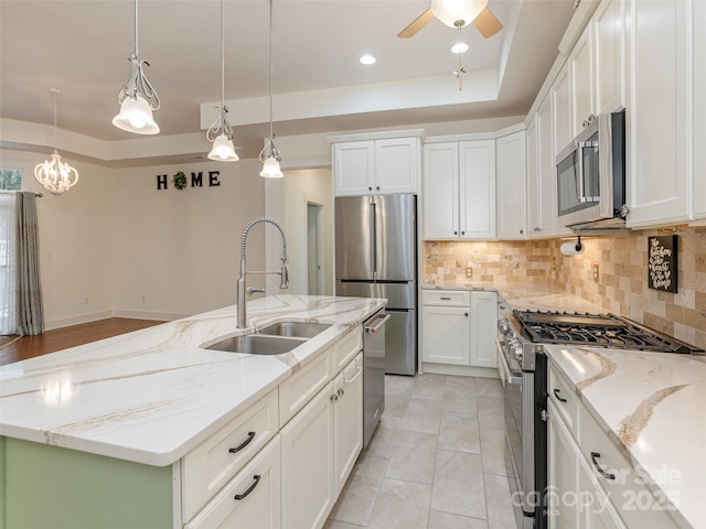 kitchen with sink, stainless steel appliances, light stone countertops, white cabinets, and a center island with sink