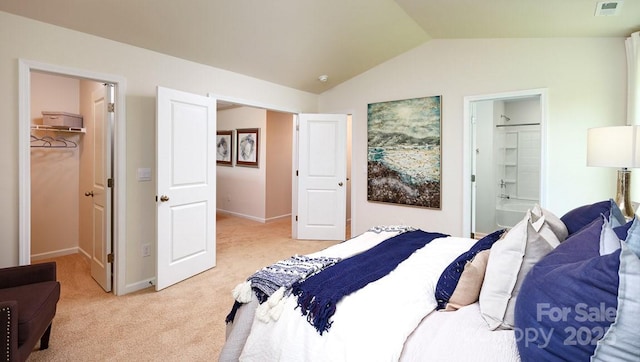 bedroom featuring vaulted ceiling, ensuite bathroom, a walk in closet, light colored carpet, and a closet