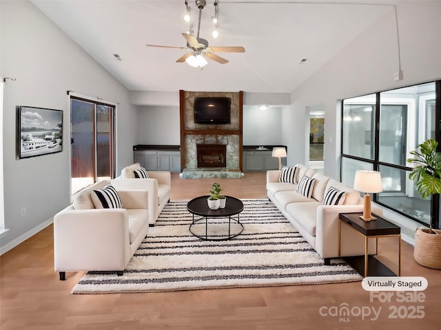 living room with vaulted ceiling, light wood-type flooring, ceiling fan, and a fireplace