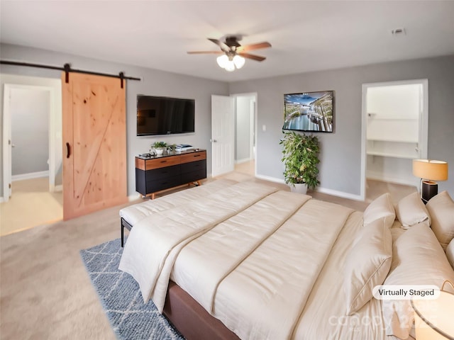 carpeted bedroom with ceiling fan, a barn door, and a spacious closet